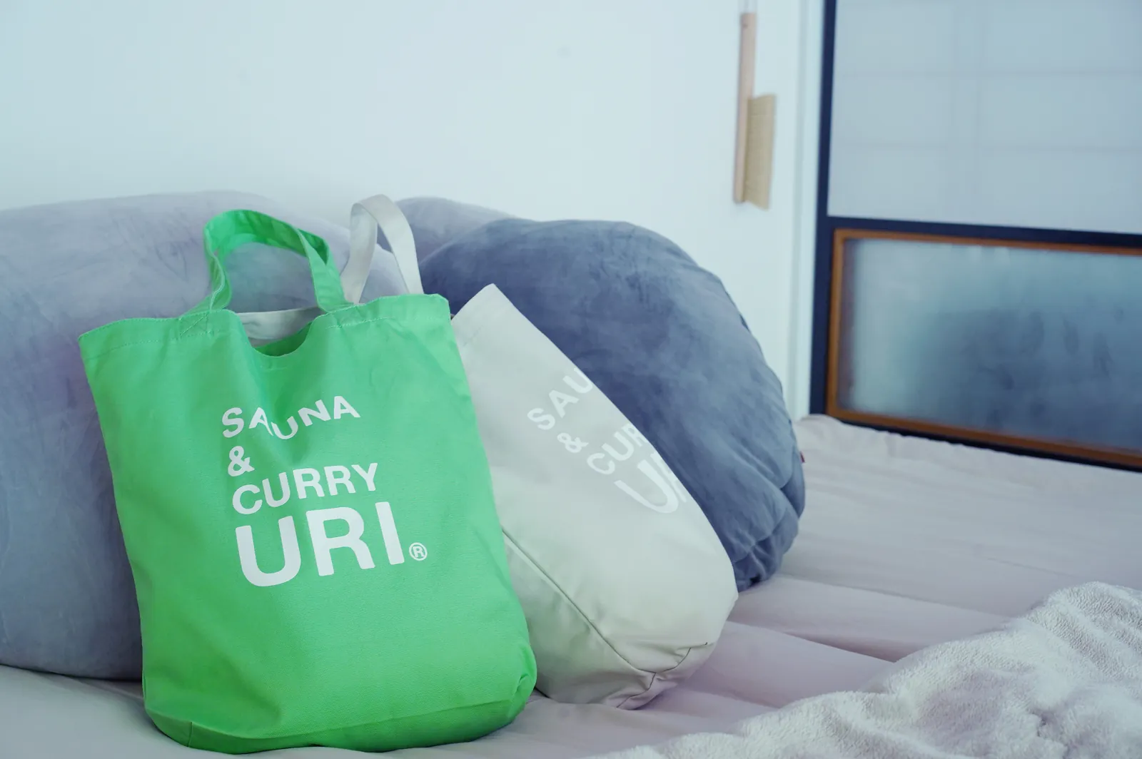栄の間のベッドに置かれたSAUNA&CURRY URIの緑のトートバッグ
