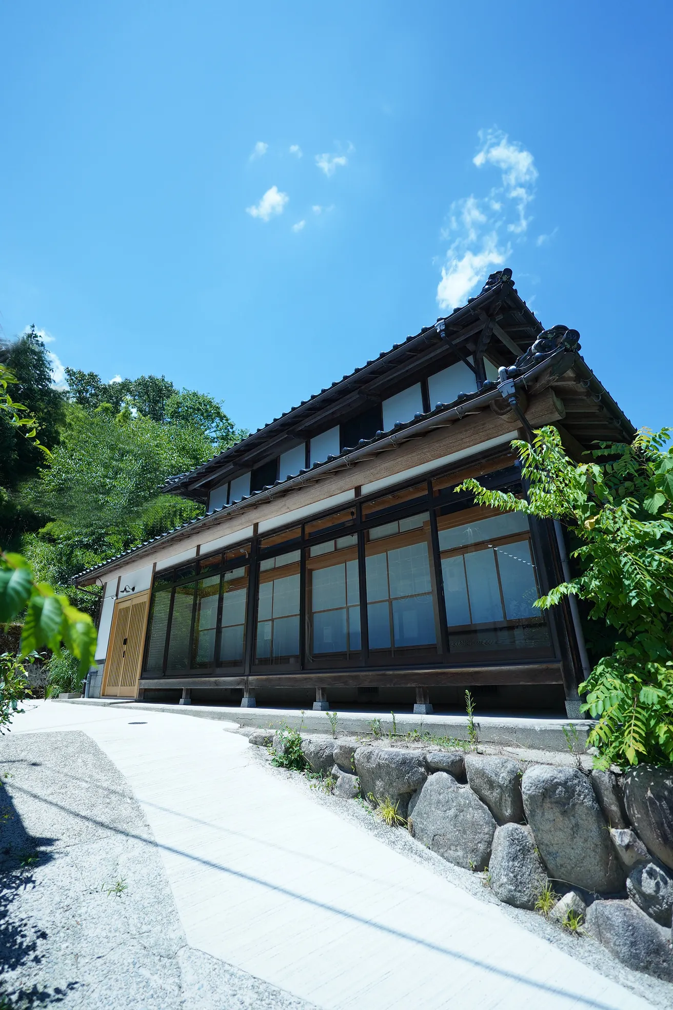 青空の下、緑に囲まれた竹の間の外観。瓦屋根の古民家